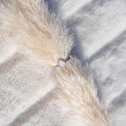 Bague goutte de lait en argent au lait maternel posée sur une plume de pampa